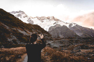 Woman photographing snow covered mountain