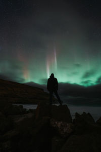 Rear view of man standing on rock at night