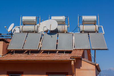 A lot of solar water heating systems on roof of house. a lot water tanks on roof.