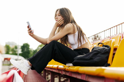 A teenage girl sits on the school bleachers and writes a message on her phone in her free time