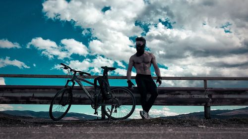 Man with bicycle on railing against sky