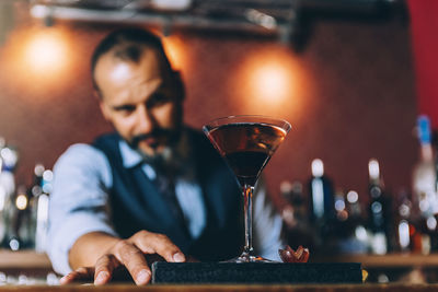 Portrait of mature bartender standing by cocktail on bar counter