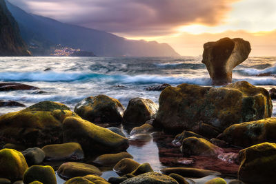 Rocks at sea shore against sky during sunset