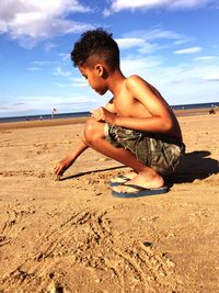 Full length of shirtless boy on sand at beach against sky