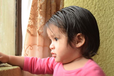 Close-up of cute girl looking through window at home