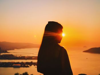 Silhouette woman looking at sea during sunrise