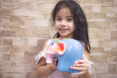 Portrait of smiling girl holding face against wall