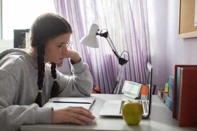 The teen is studying remotely via the internet using a laptop.