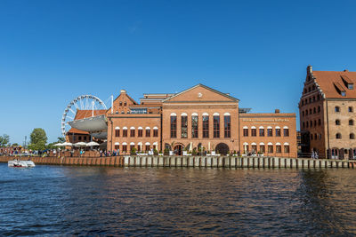 View of buildings by river against blue sky