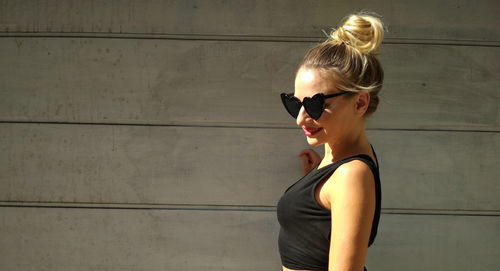 Woman wearing sunglasses standing against wall