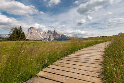 Wooden hiking trail at seiser alm with sassolungo mountain group in front of blue sky with clouds
