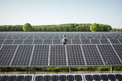 Mature man using smartphone standing on panel in solar plant