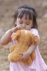 Portrait of cute girl holding teddy bear while standing outdoors