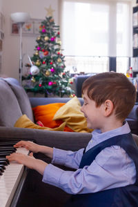 Boy sitting playing piano at home at christmas