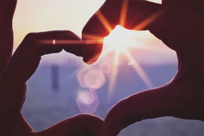 Cropped image of person making heart shape against sky