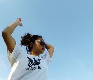 Low angle view of woman holding umbrella against blue sky