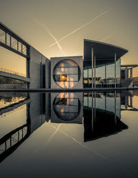 Symmetry view of buildings by artificial pond against sky during sunset