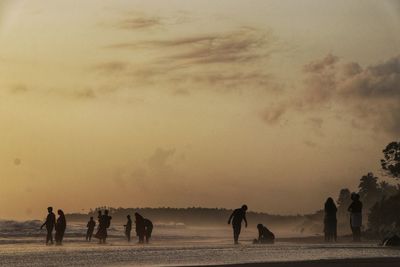 Group of people at beach against sky during sunset
