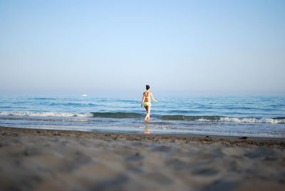 Rear view of woman walking at beach against clear sky