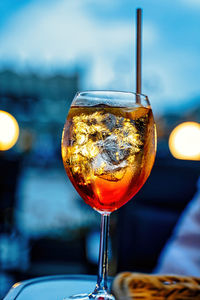 A cold alcoholic beverage aperol spritz with ice and straw against out of focus background