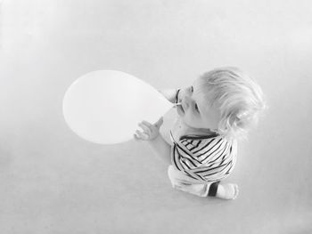 High angle view of baby boy biting balloon against gray background