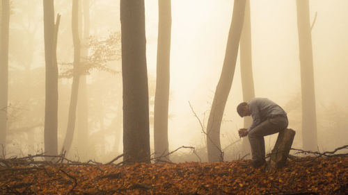 Side view of depressed man sitting on tree stump in foggy forest