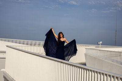 Woman sitting on railing against the sky