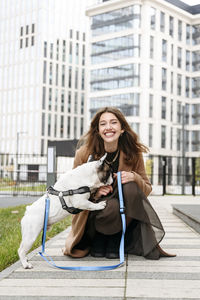 Happy woman playing with french bulldog on footpath