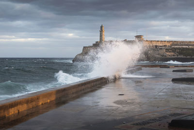 Sea waves splashing on shore against sky