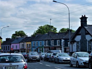 Cars on street by buildings in city against sky