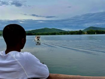 Rear view of man looking at lake against sky