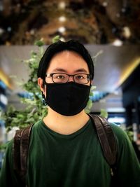 Portrait of young man wearing eyeglasses and face mask in mall arcade.