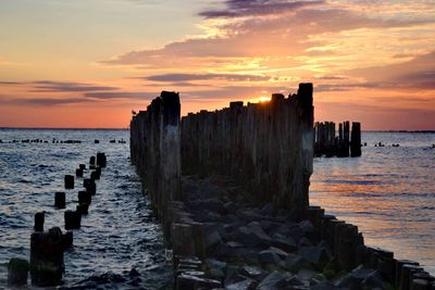 Wooden posts on sea against sky during sunset