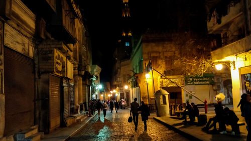 People walking on illuminated street amidst buildings at night