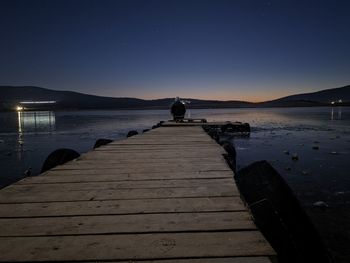 Man sitting on pier over lake against sky at night