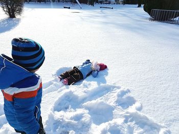 High angle view of boy looking at friend lying down on snow covered field