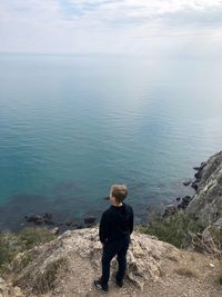 Rear view of boy standing on sea shore against sky