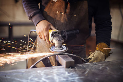 Craftsperson using circular saw while polishing metal at factory