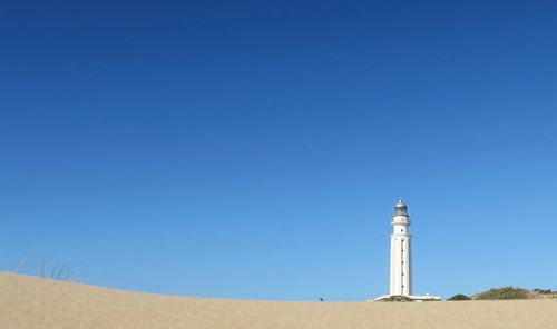 Lighthouse on beach against clear blue sky