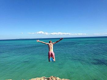 Young woman jumping on sea against blue sky