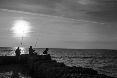 Silhouette men fishing in sea