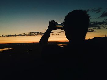Silhouette man holding camera against sky during sunset