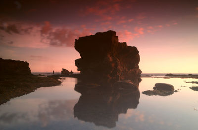 Reflection of rock on sea against sky during sunset