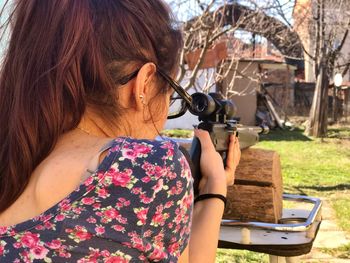 Rear view of young woman shooting weapon at backyard