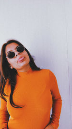 Portrait of young woman wearing sunglasses standing against wall