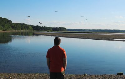 Rear view of man standing at lakeshore against sky