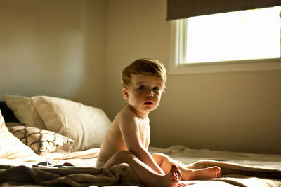 Portrait of cute shirtless boy sitting on bed at home