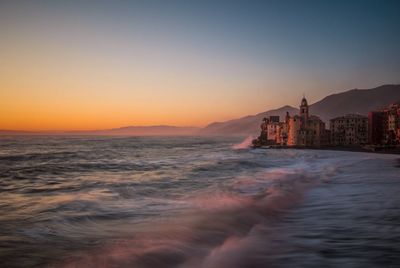 Buildings by sea against sky during sunset