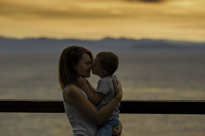 Mother with daughter against sky during sunset