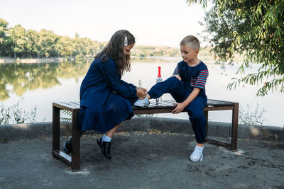 Little girl helps boy brother tie shoelace on bench in park. sister tying laces on shoes brother